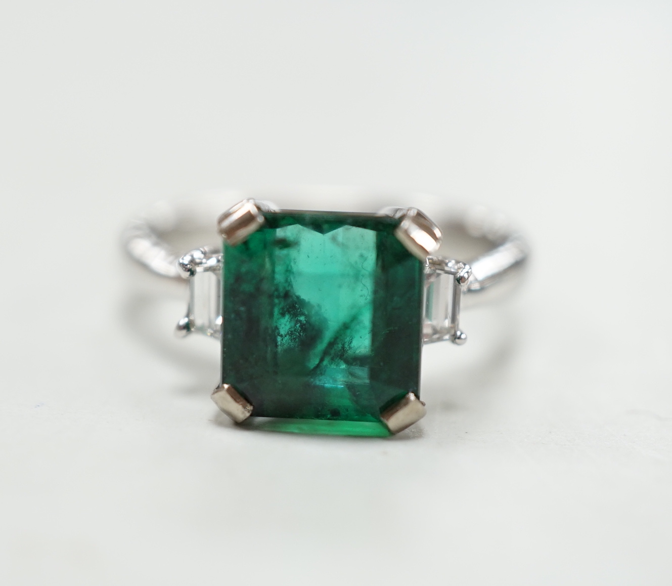 A modern 18k white metal and single stone emerald set ring, baguette cut diamond set shoulders, size N, gross weight 5.8 grams